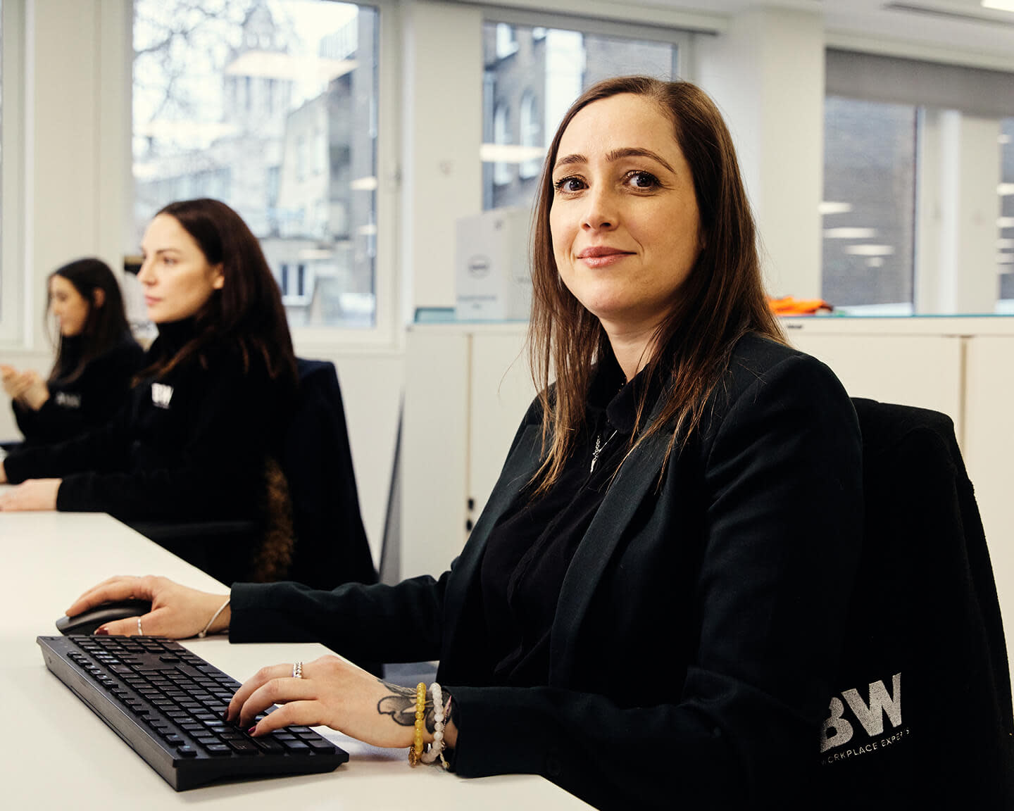 Woman in black jacket working at a keyboard in a bright office setting