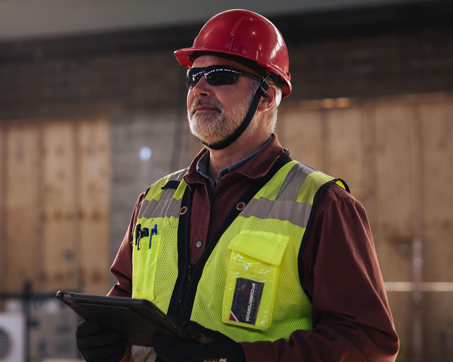 Construction worker wearing red helmet and yellow vest holding a tablet