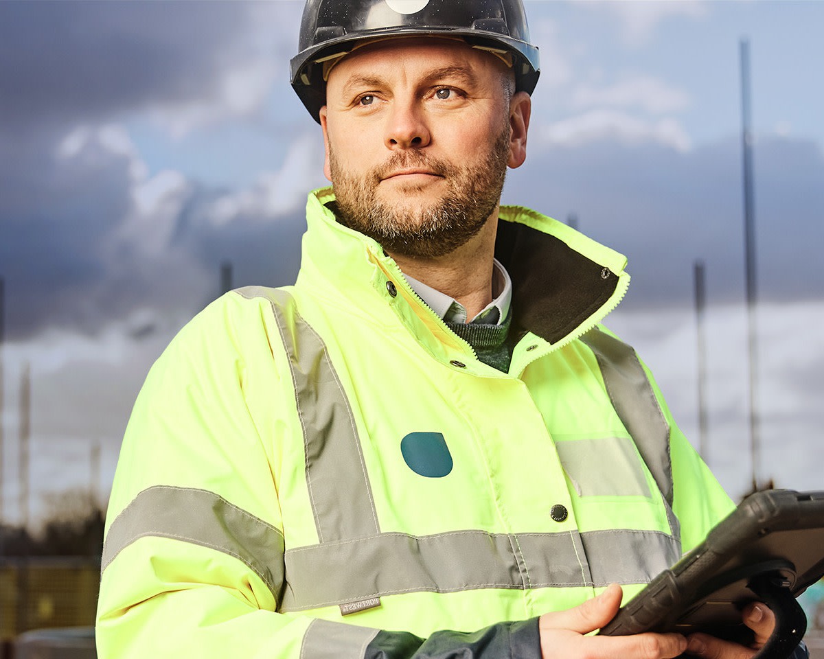 Construction worker wearing red helmet and yellow vest holding a tablet